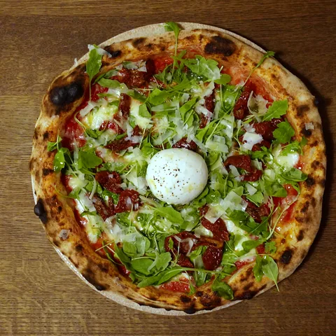 Burrata sapnis — pica ar burratu, saulē kaltētiem tomātiem un rukolu, skats no augšas